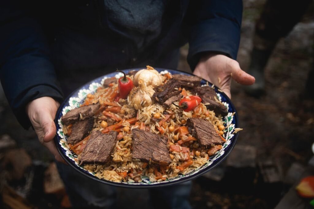 A flavorful plate of beef and rice pilaf with vegetables cooked outdoors, served with garnishes.