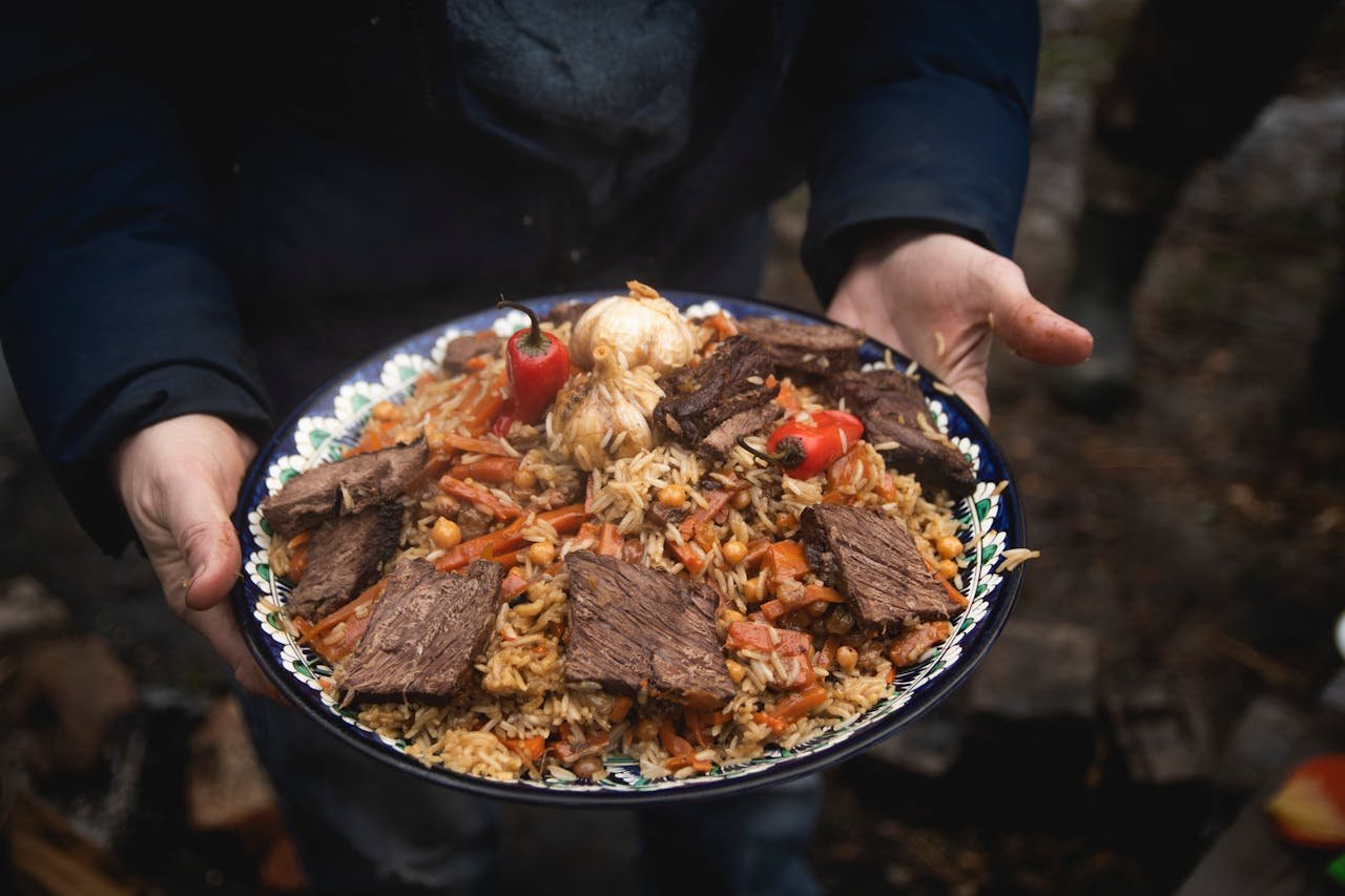 A flavorful plate of beef and rice pilaf with vegetables cooked outdoors, served with garnishes.